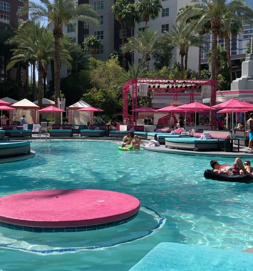 A pool with pink umbrellas and turquoise tanning beds