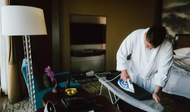 A man irons his cloths in the hotel room.