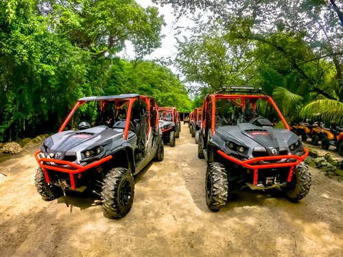 Happy travelers enjoying an ATV ride through the jungle in Cozumel, Mexico, during a Riviera Maya itinerary shore excursion, splashing through muddy water for an adventurous experience.